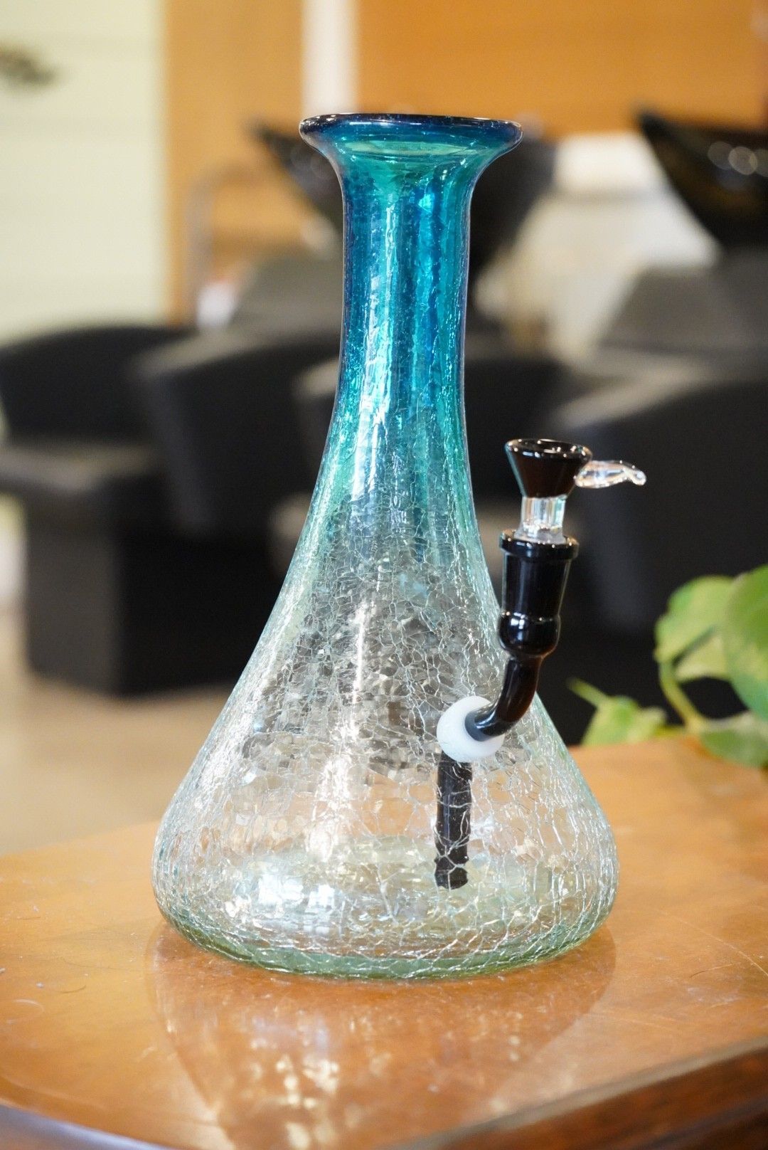 Blue glass water pipe on a wooden table, with a black metal downstem and blurred background.