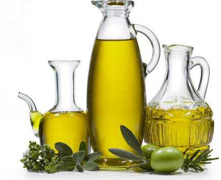 Three glass cruets filled with golden olive oil, accented with fresh olives and herbs on a white background.