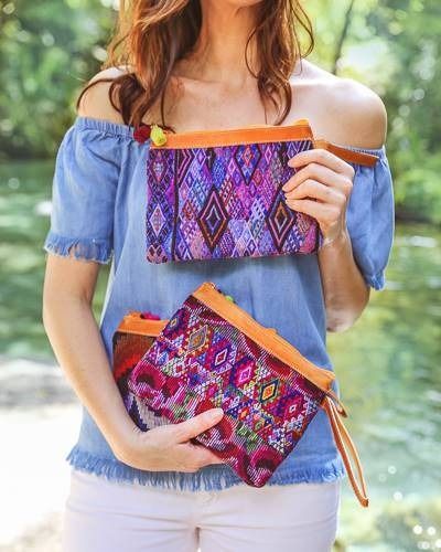 A person holding two vibrant, patterned zippered pouches with brown leather accents against a blurred outdoor backdrop.
