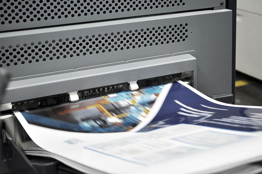 Pile Of Papers On Printing Machine During Production — Graphic Designer In Airlie Beach, QLD