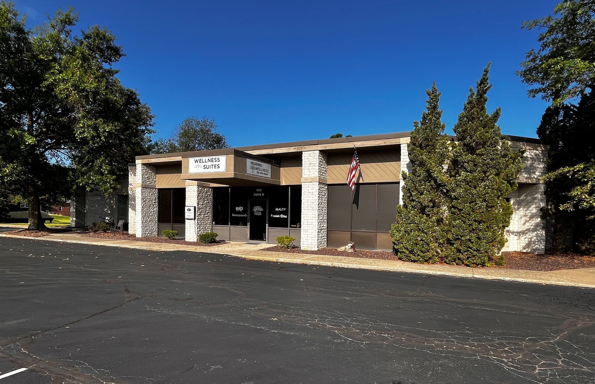 A building with a stone facade has a centered entrance and windows, reads Hearing Wellness on the front.