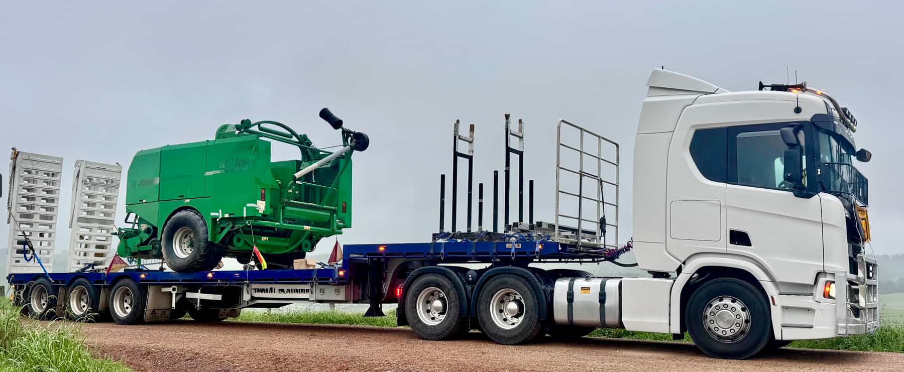 A White Semi Truck is Carrying a Green Combine Harvester on a Trailer — Goulburn Transport In Adelaide, SA