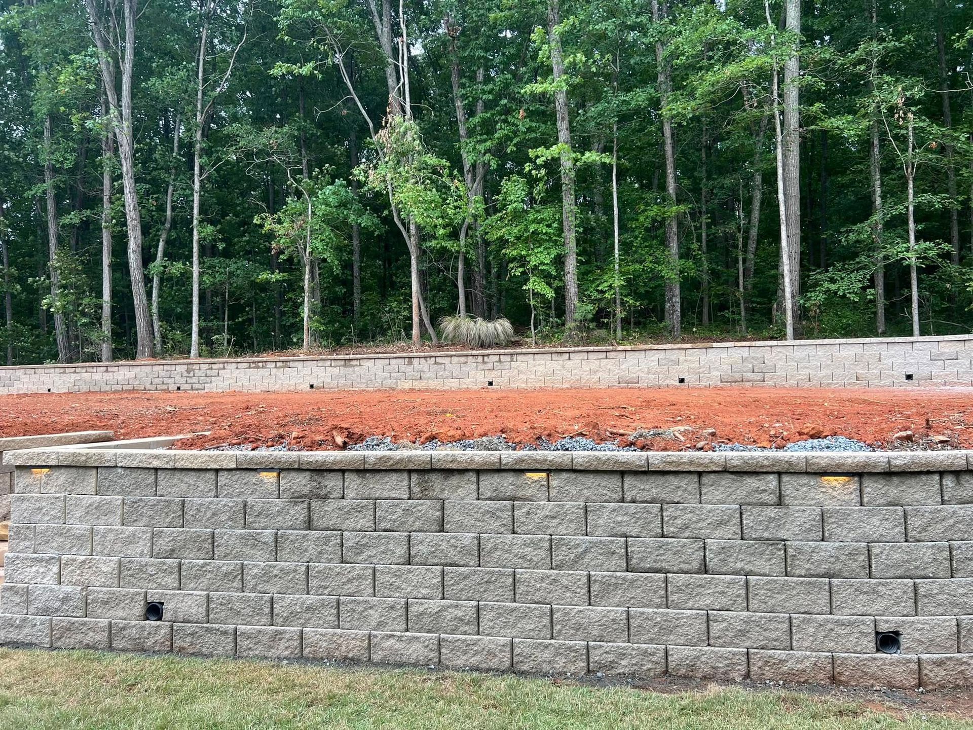 Stone retaining wall with red soil in front of a wooded background