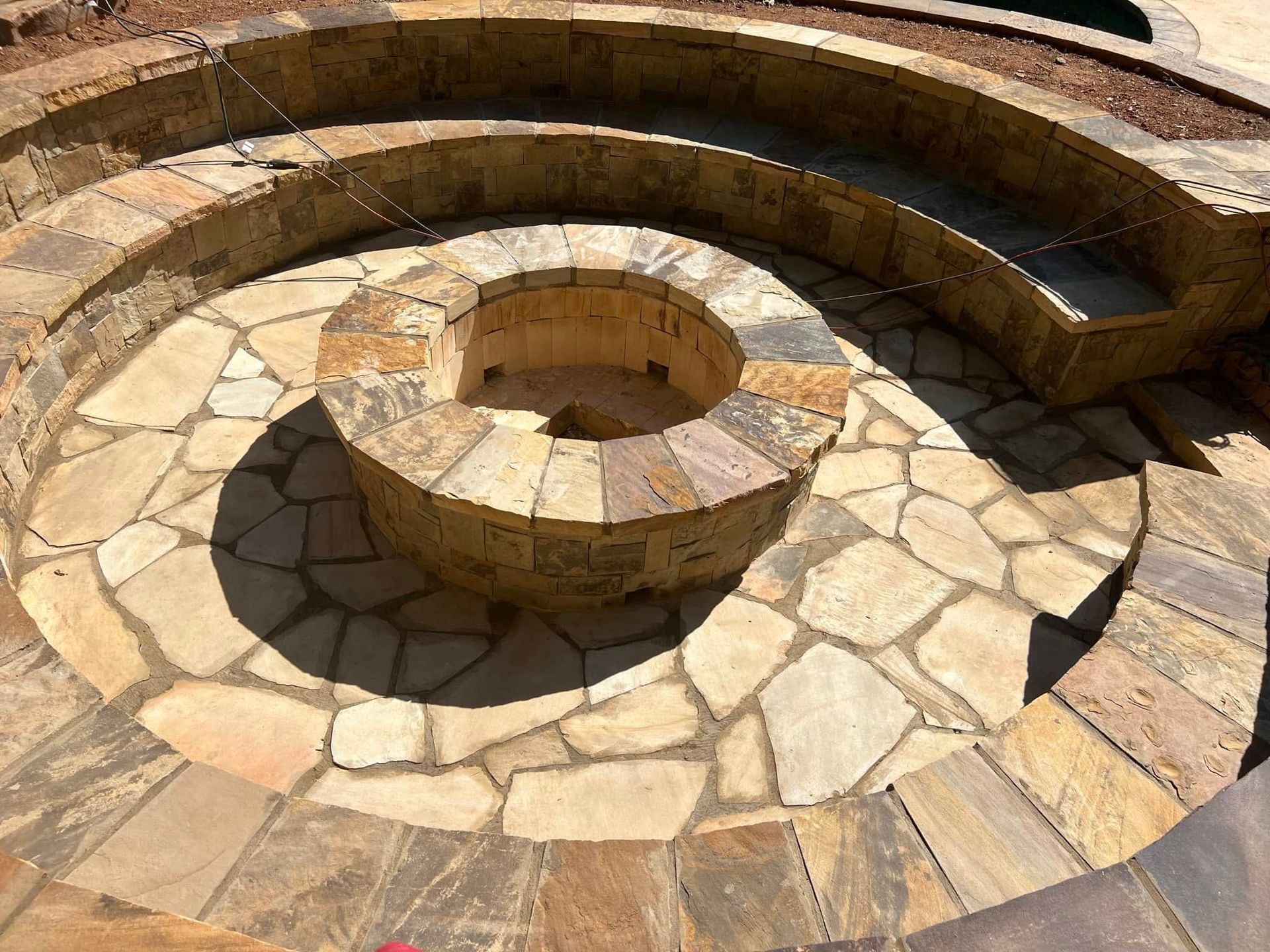 Circular stone fire pit with built-in curved benches on a tiled patio in sunlight