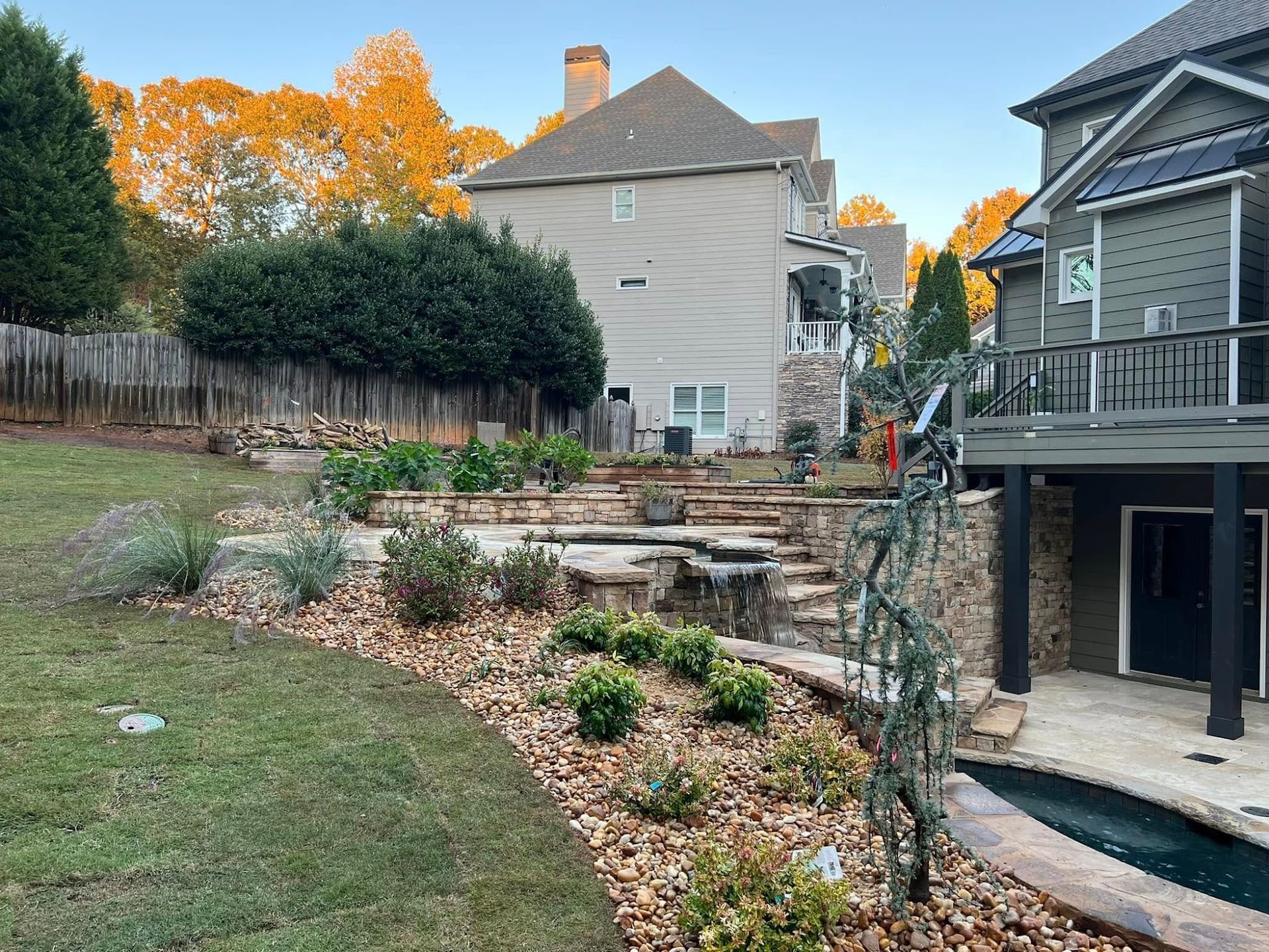 Backyard with stone terraced garden beds, a grassy slope, and a house deck on the right at sunset
