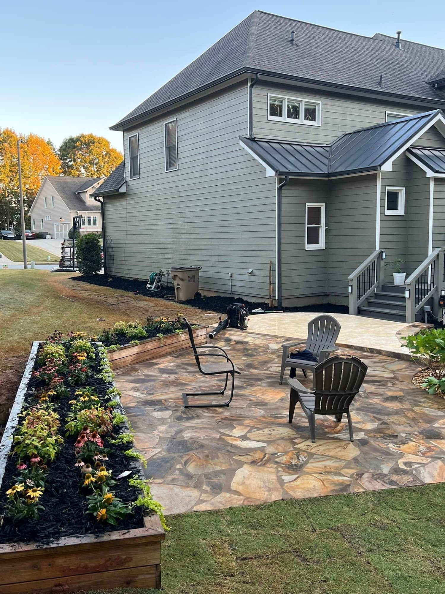 Backyard stone patio with flower bed, outdoor chairs, and a gray house exterior
