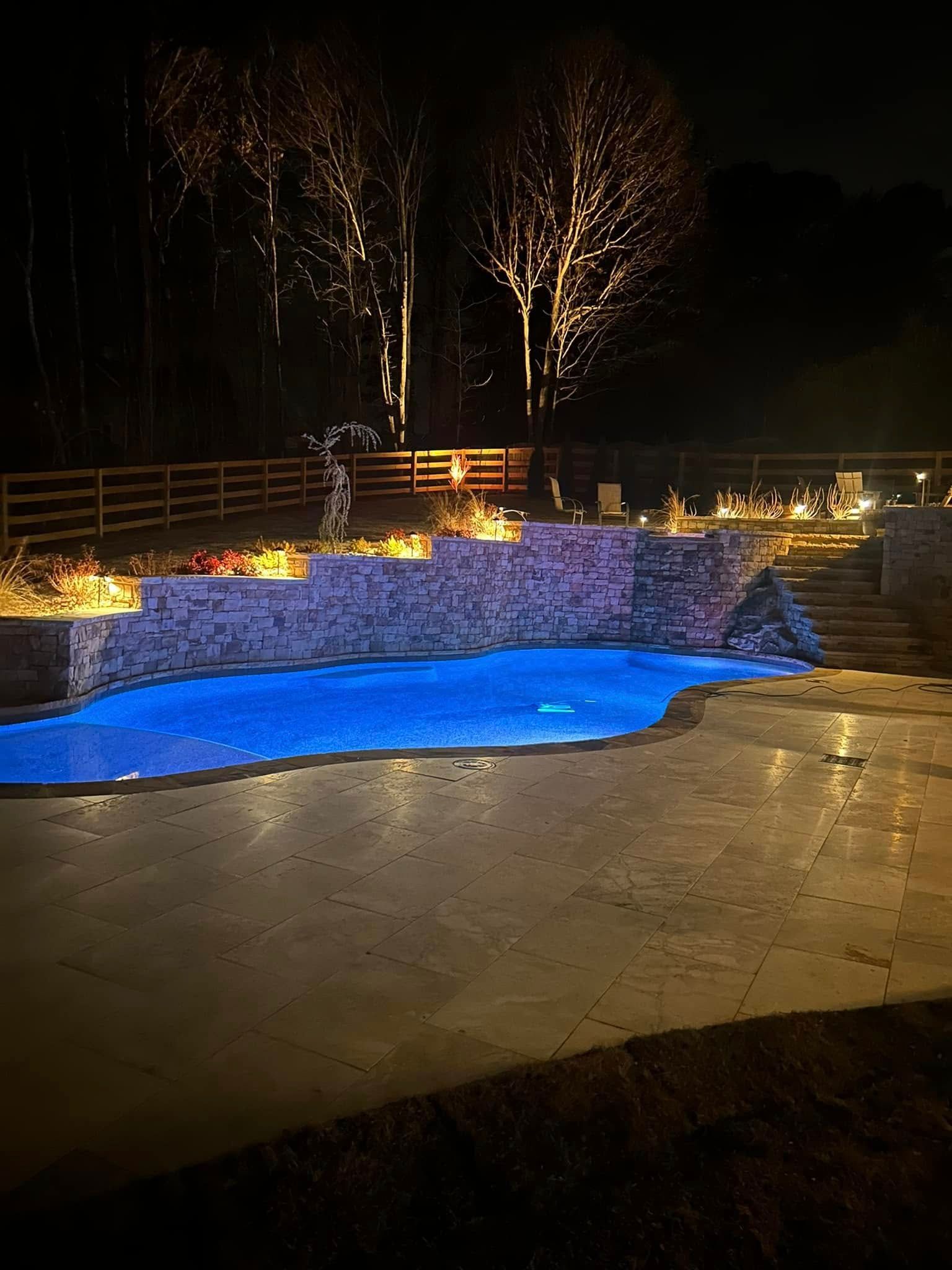 Nighttime lit fountain with glowing blue water and warm lights along a stone pool.