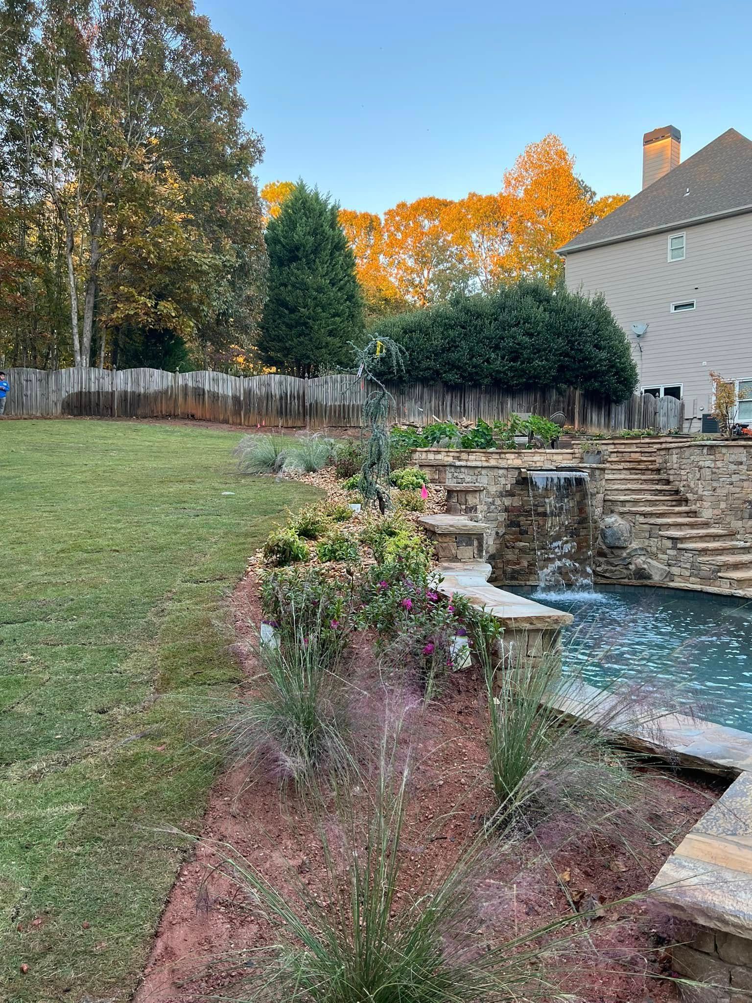 Backyard garden with stone steps, a small pool, and autumn-colored trees at dusk