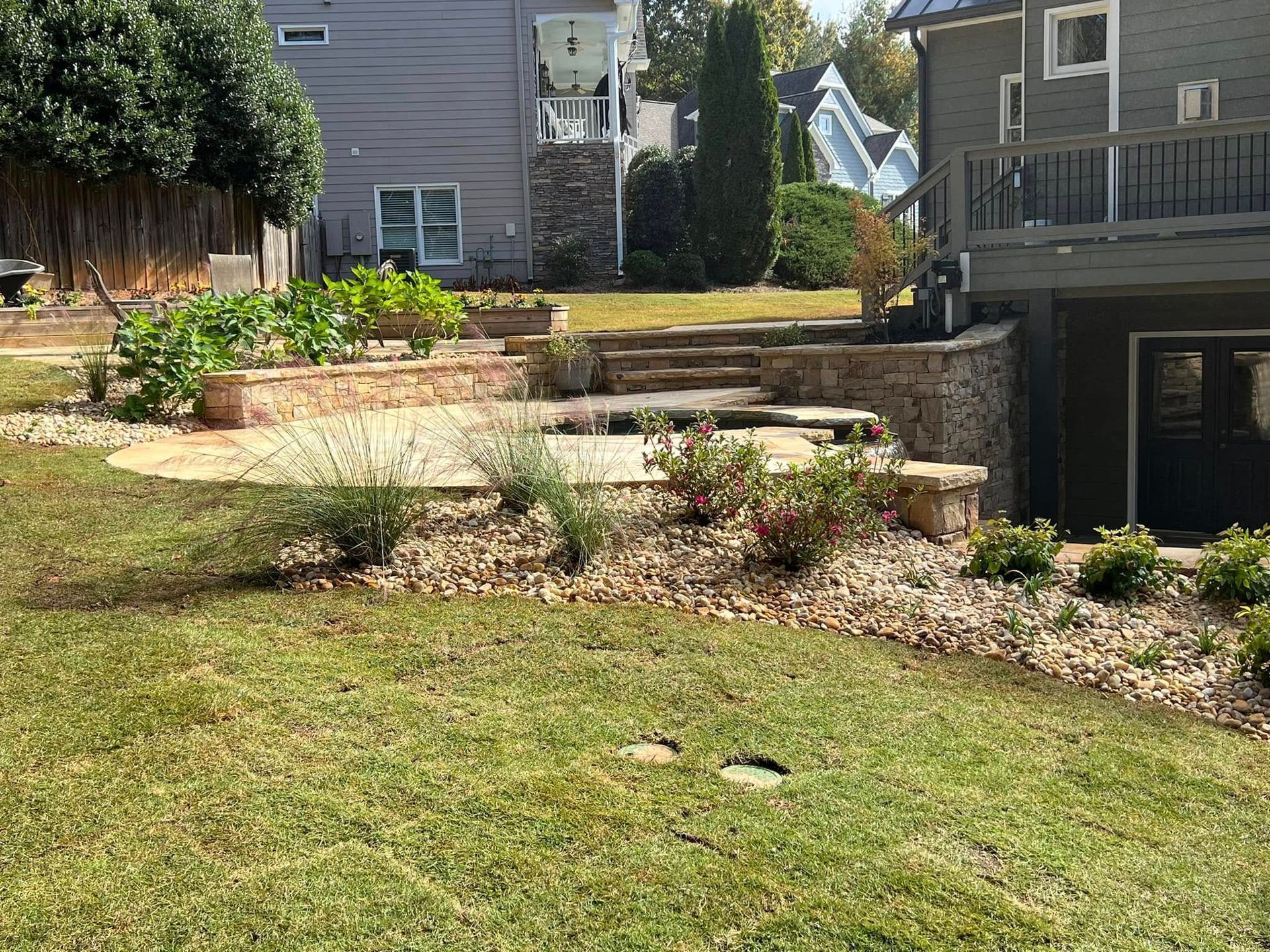 Backyard terraced garden with stone retaining walls and a green lawn beside a house