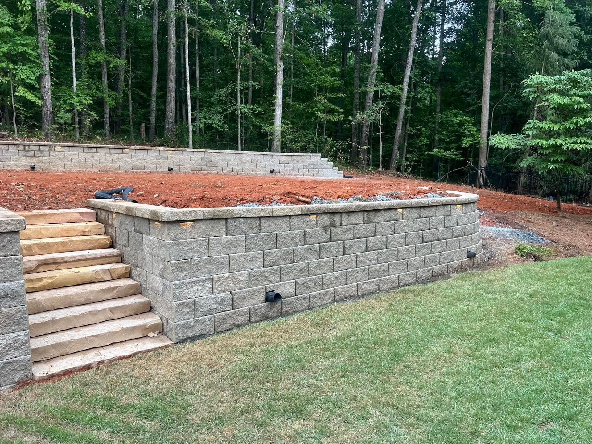 Stone retaining wall with stairs beside a raised yard in a wooded backyard