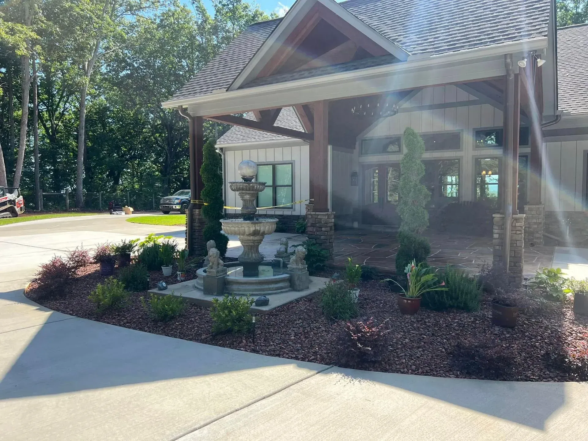 Landscaped building entrance with stone fountain, shrubs, and a covered porch in bright sunlight