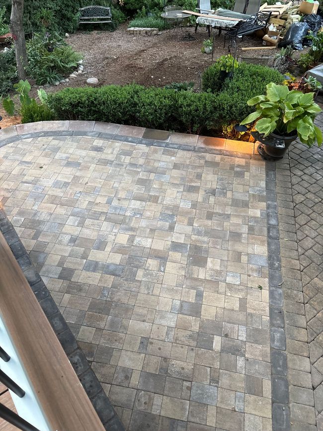 Back patio with stone pavers, garden bed, and glowing fire feature beside green plants