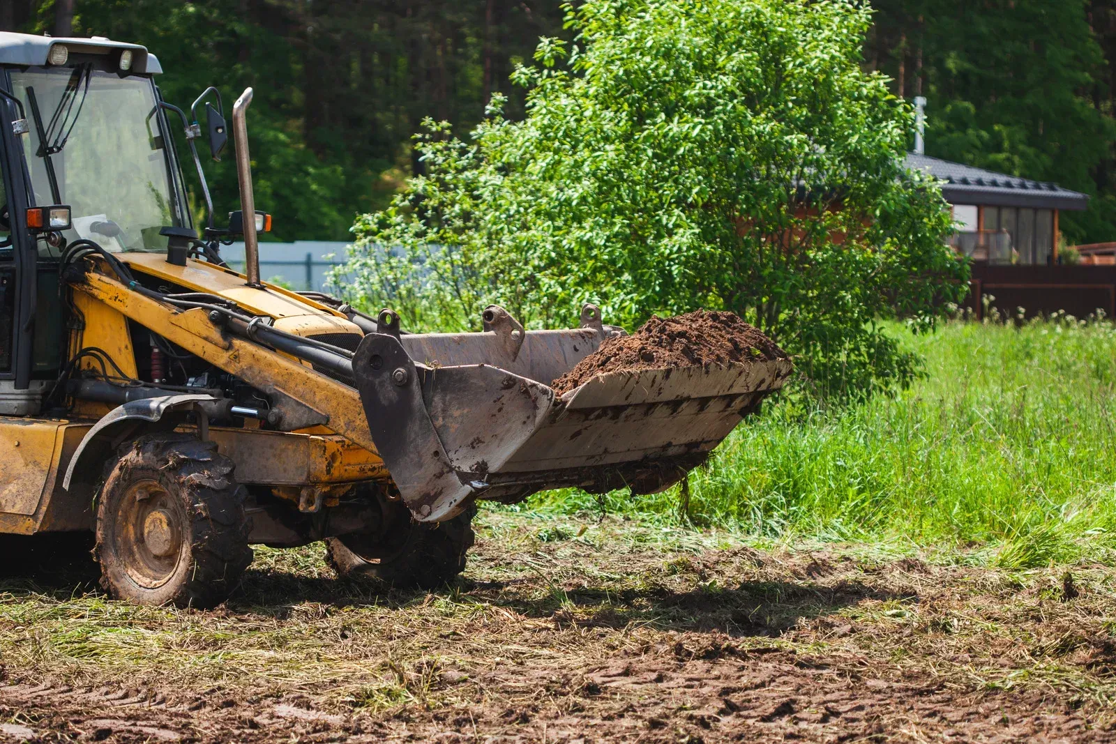 Red excavator clearing tangled roots and brush in a dusty wooded area.