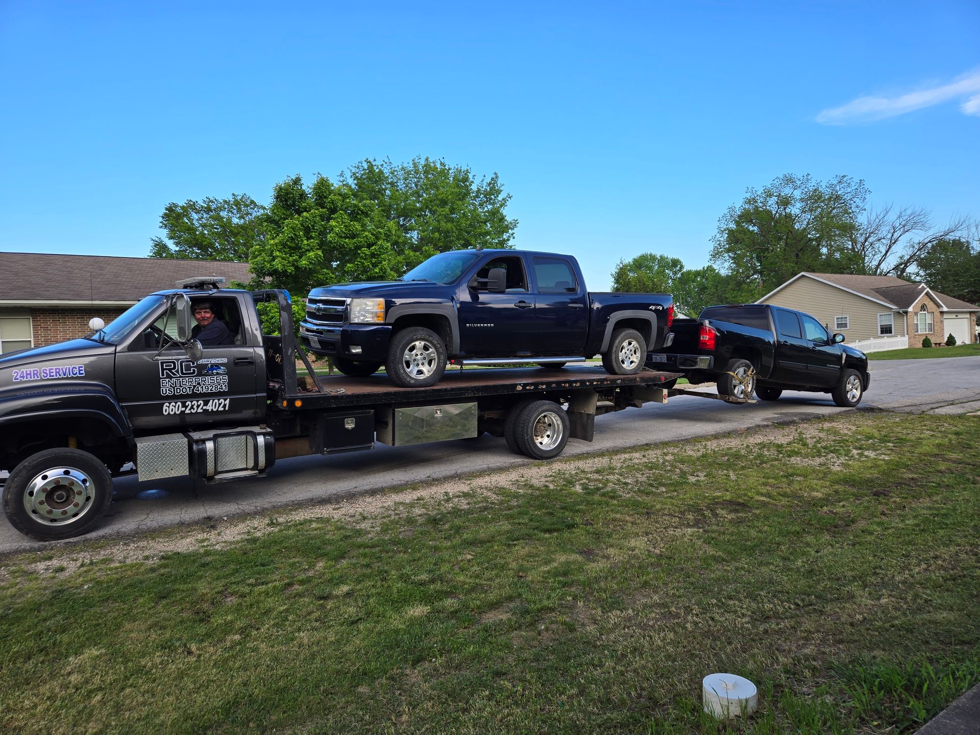 Tow truck carrying two vehicles on a residential street. One truck is loaded, the other is being towed.