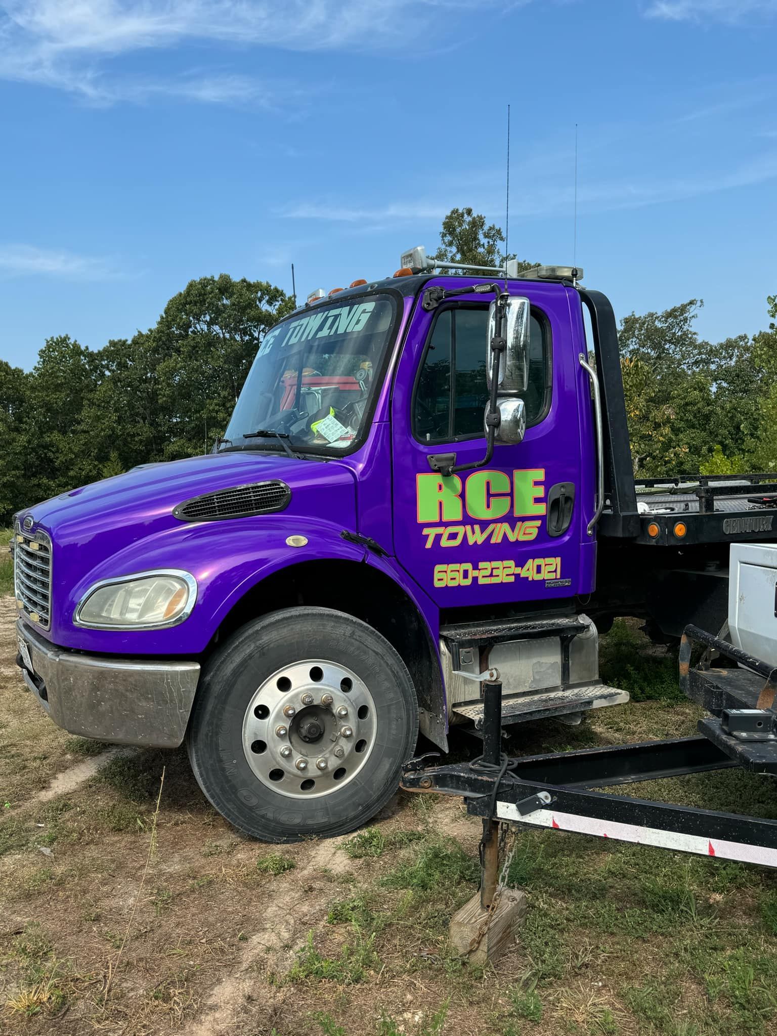 Purple tow truck parked outdoors with green logo.