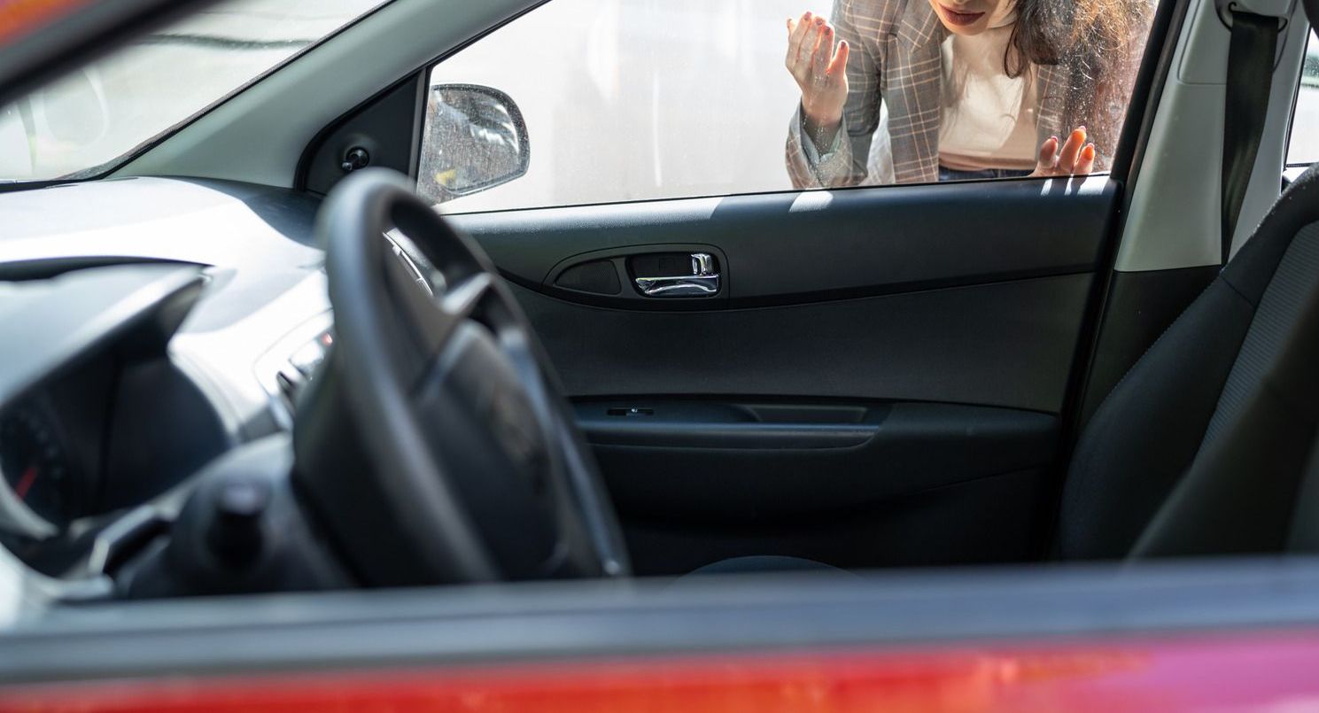 Woman locked out of a red car, looking frustrated.