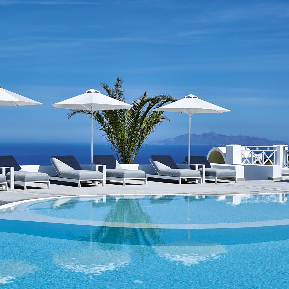 Piscina di lusso in un resort con lettini, ombrelloni bianchi e vista sull'oceano sotto un cielo azzurro limpido.