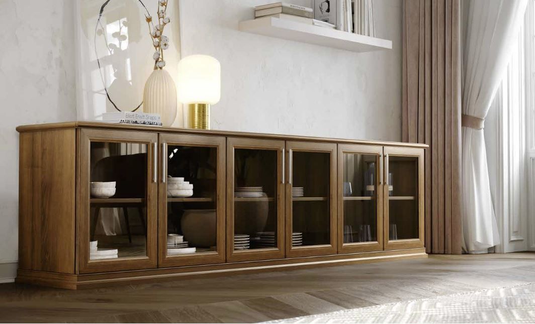 Credenza in legno con ante in vetro in un luminoso soggiorno, sormontata da una lampada, un vaso e decorazioni.