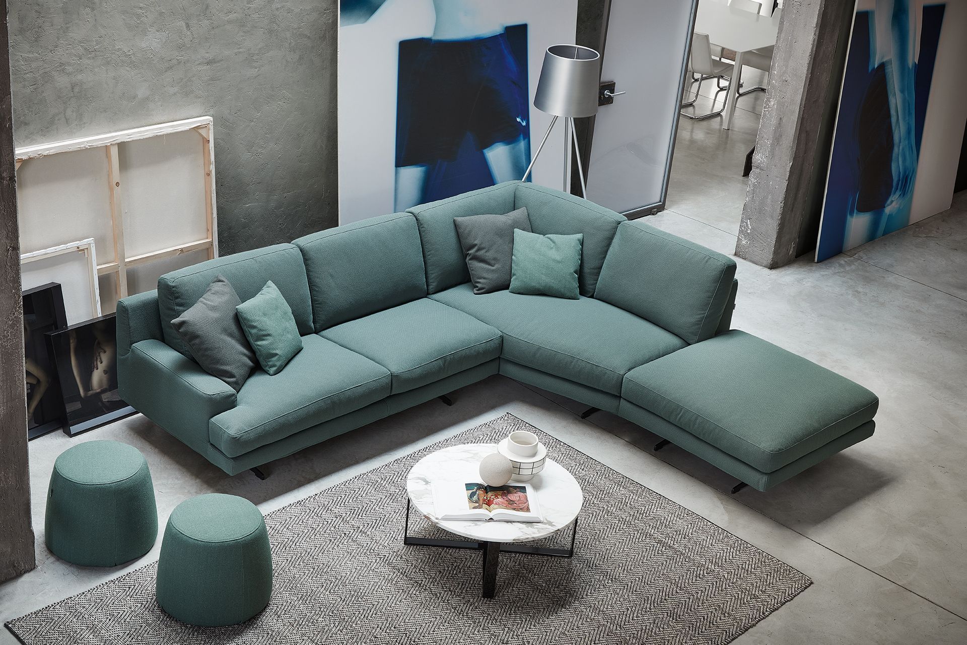 Soggiorno moderno con divano componibile color verde acqua, tavolino rotondo bianco, pouf e tappeto a motivi geometrici.