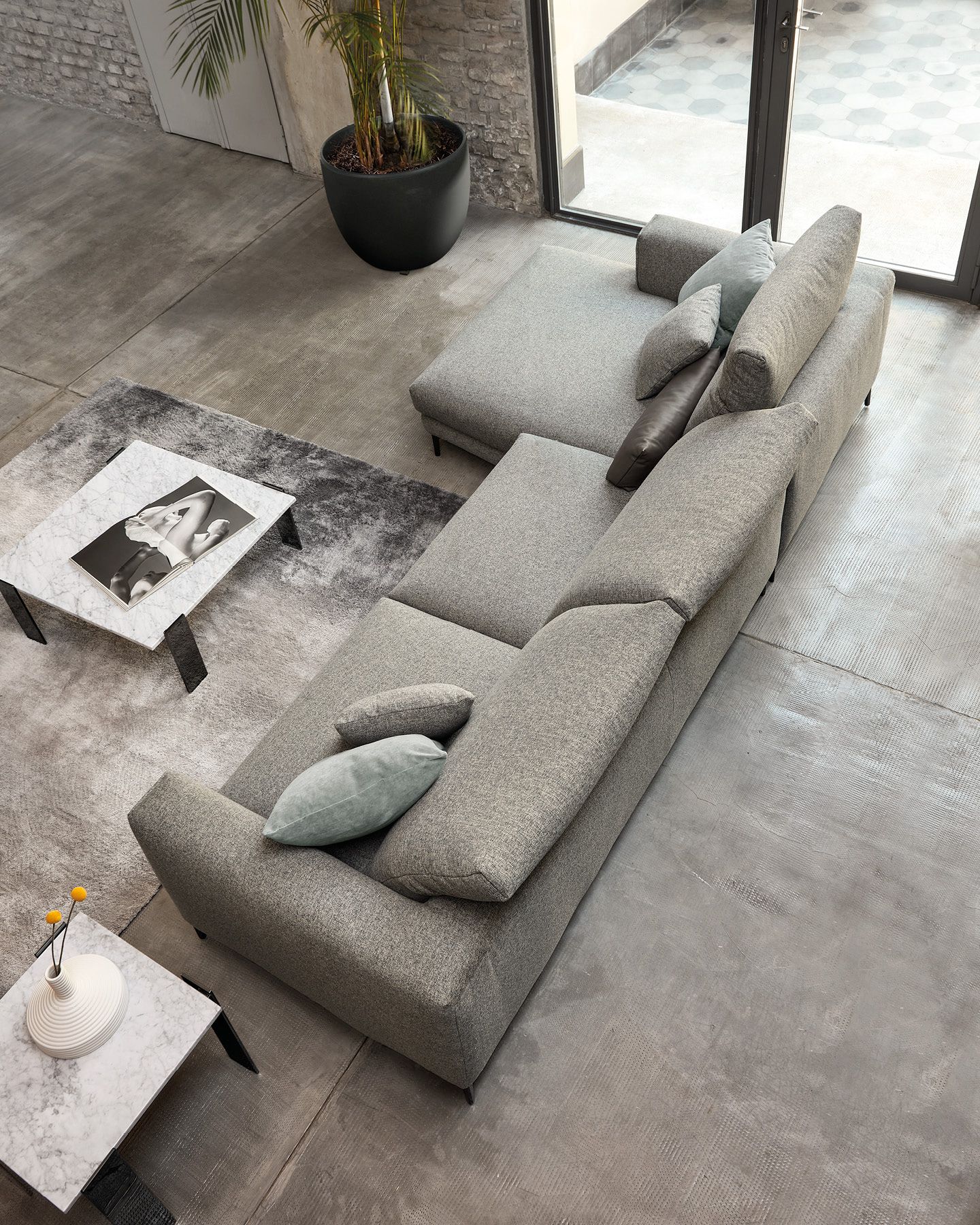 Soggiorno moderno con divano componibile grigio, pouf abbinato, tavolino da caffè e tappeto vicino alle grandi finestre.