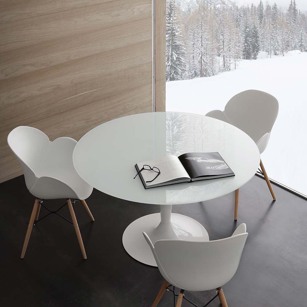 Angolo pranzo moderno con tavolo rotondo bianco, quattro sedie bianche e vista sulla foresta innevata all'esterno.