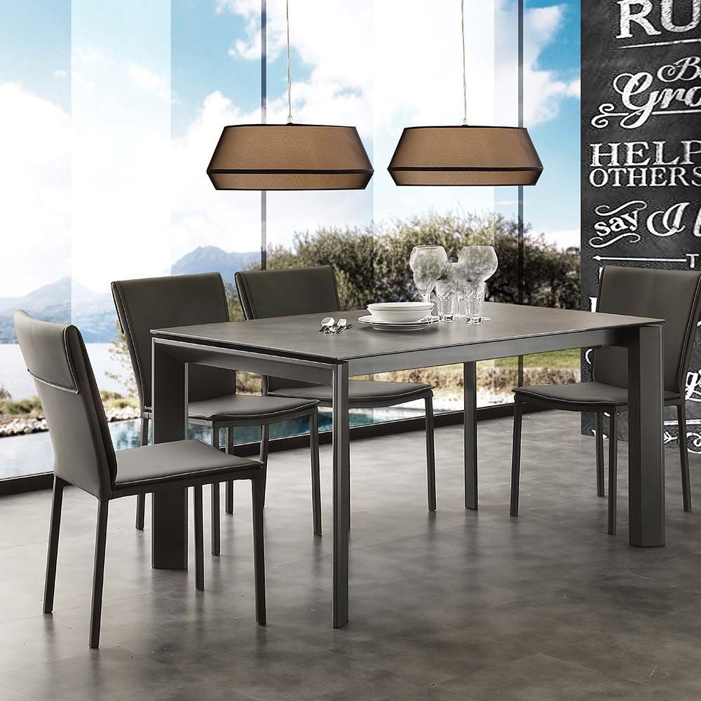 Tavolo da pranzo moderno con sedie scure e lampade a sospensione in una stanza luminosa con ampie finestre.