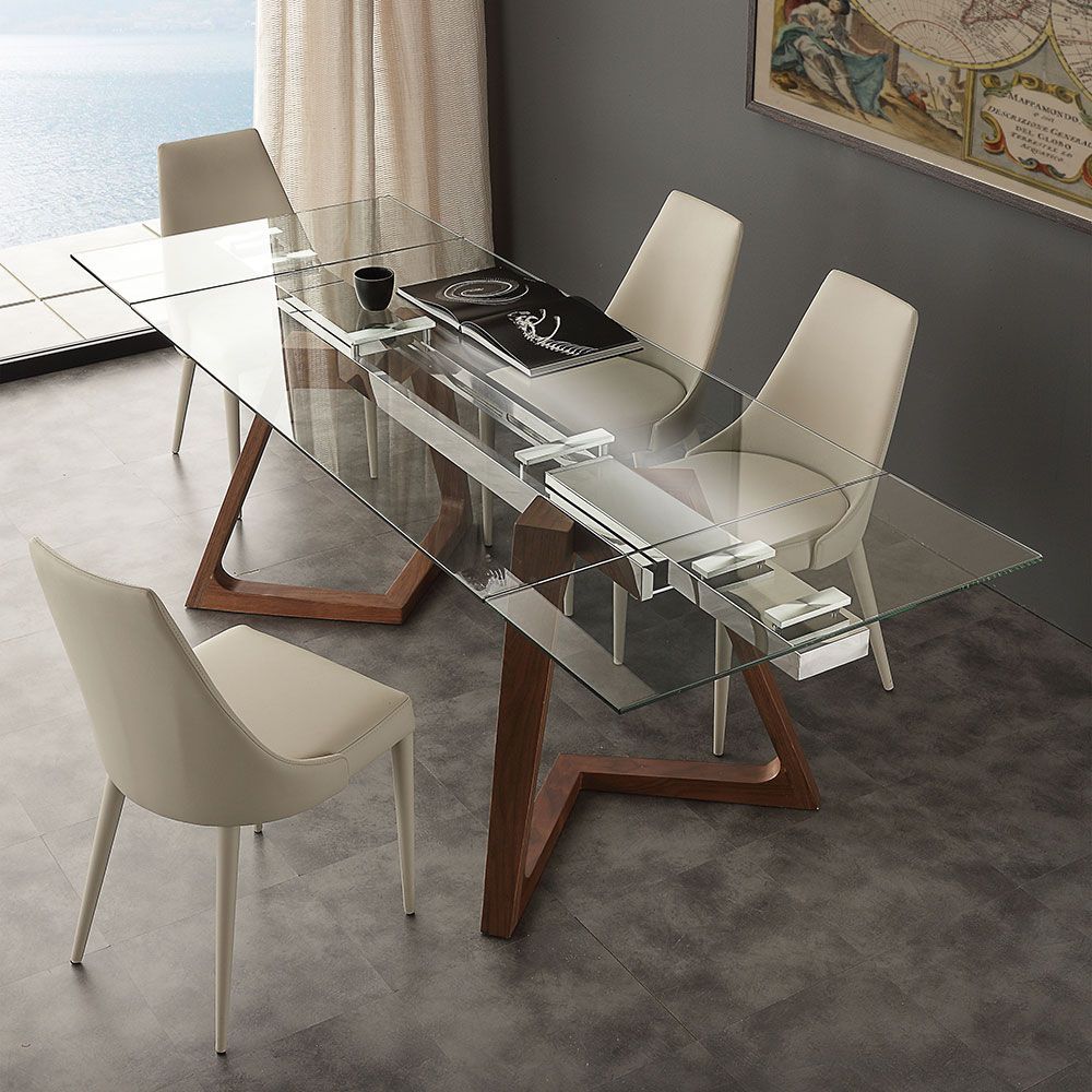 Tavolo da pranzo moderno con piano in vetro, base in legno e quattro sedie color crema in una stanza luminosa.