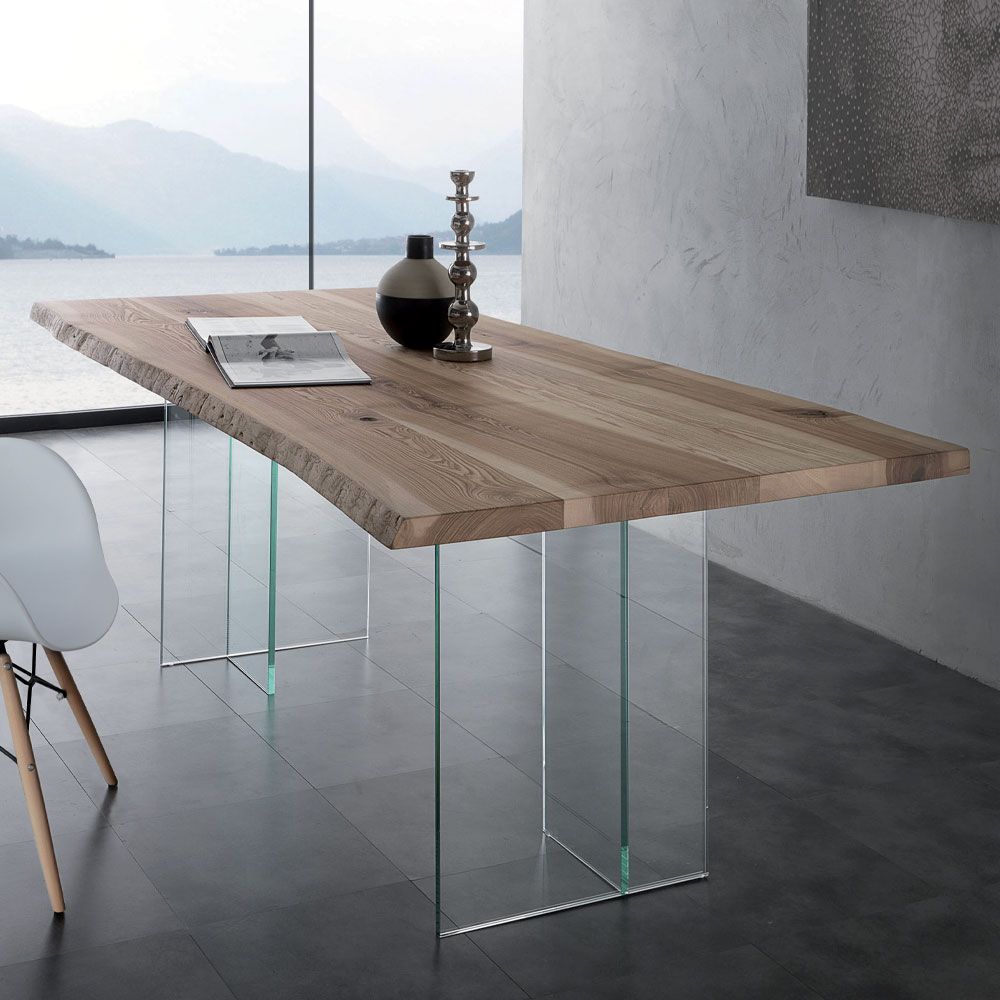 Scrivania moderna in vetro con piano in legno in una stanza minimalista, su cui sono appoggiati un libro e un vaso.