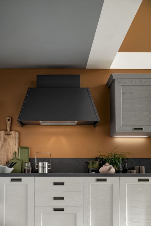 Cucina moderna con cappa nera, mobili bianchi e parete decorativa marrone.