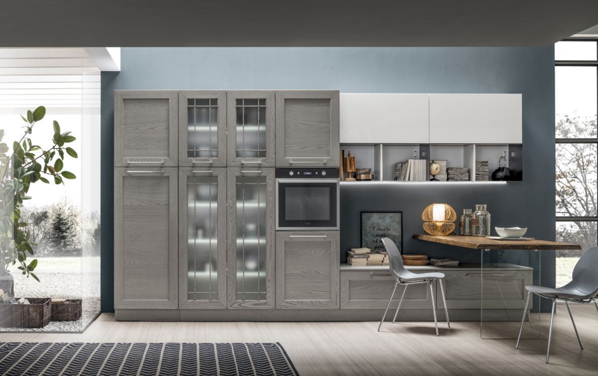 Cucina moderna grigia con pensili alti, elettrodomestici a incasso e un angolo pranzo in legno accanto a grandi finestre.