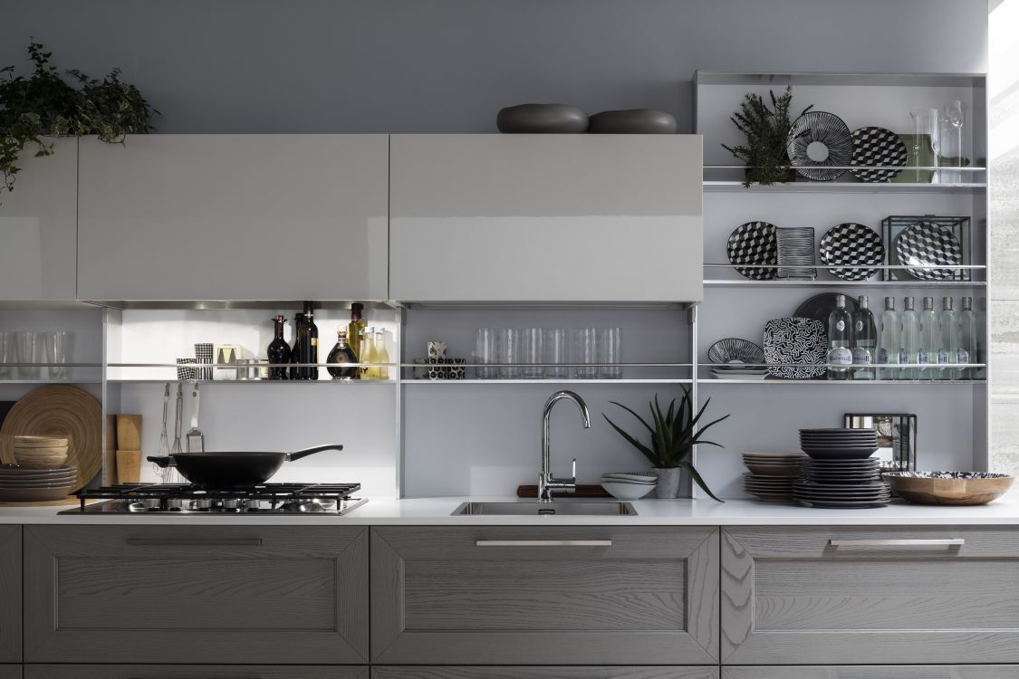 Cucina moderna grigia con mensole a vista, mobili bianchi, lavello, piano cottura e bicchieri disposti ordinatamente.