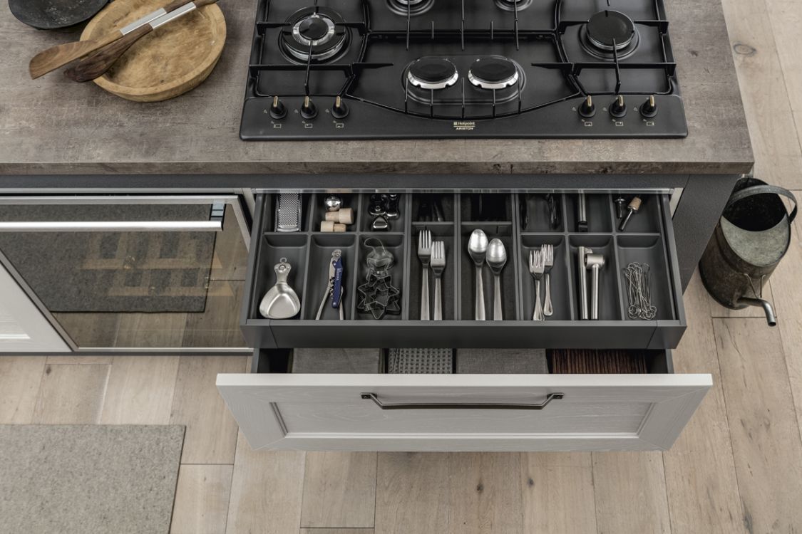 Cassetto della cucina aperto con utensili organizzati accanto a un piano cottura a gas nero su un ripiano chiaro.