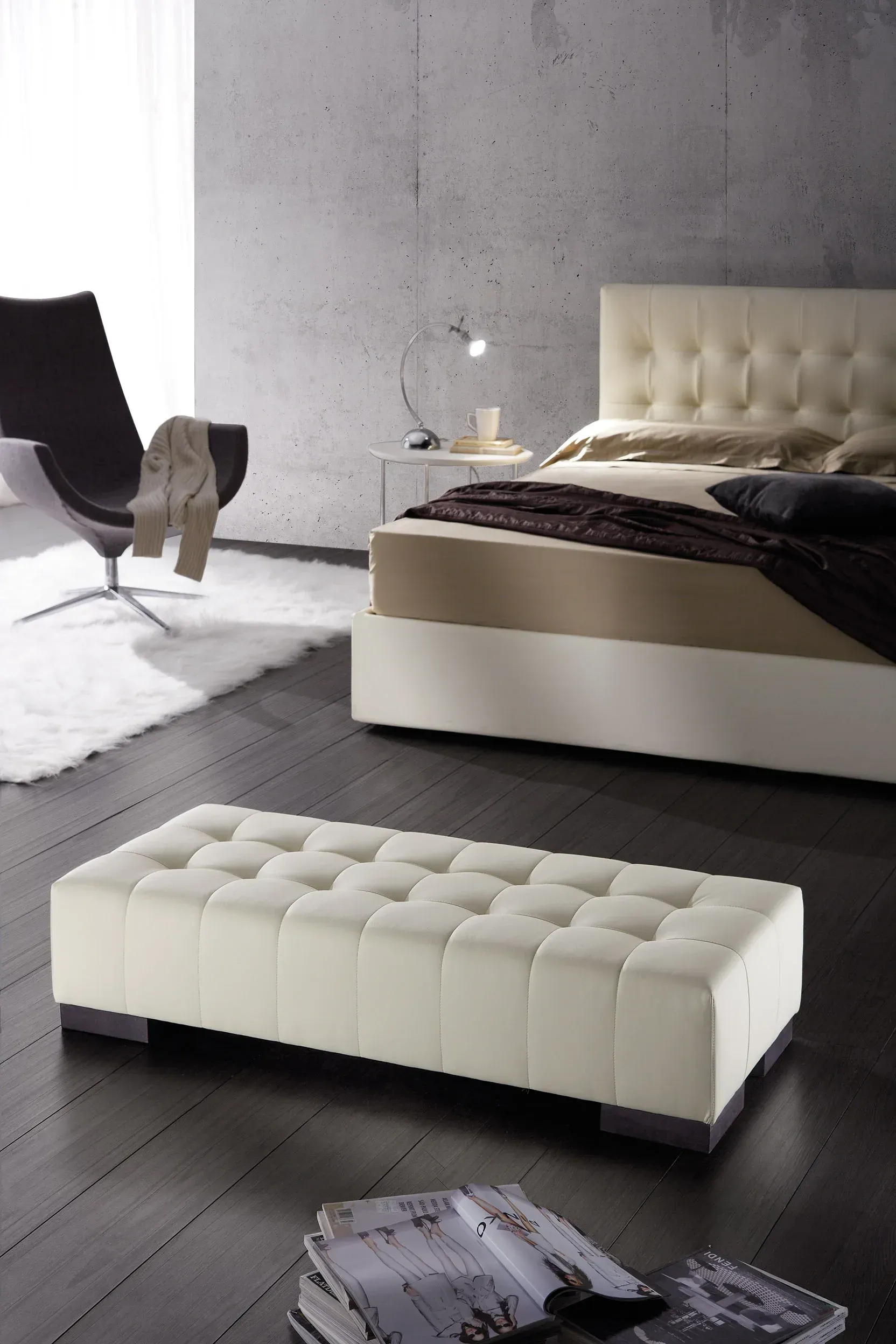 Camera da letto moderna con letto imbottito beige e pouf abbinato su un pavimento scuro, sedia nera accanto a una parete grigia.