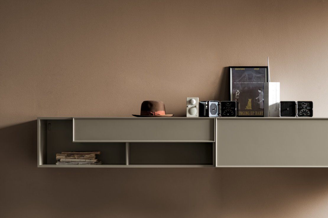 Mensola minimalista a muro con libri, un cappello e piccoli oggetti decorativi, su una parete beige.