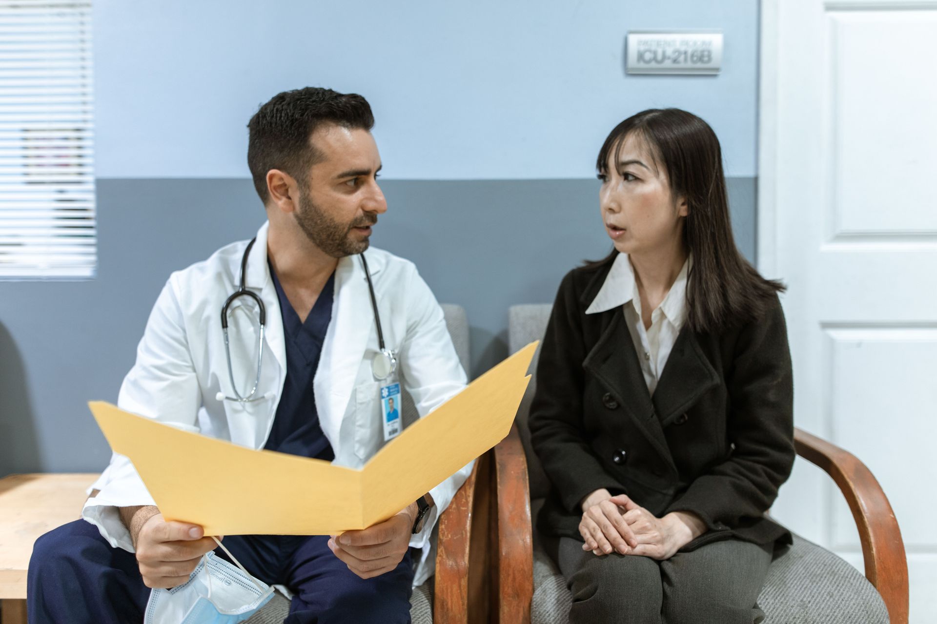 Doctor and patient seated in a clinic, talking while reviewing a yellow folder.