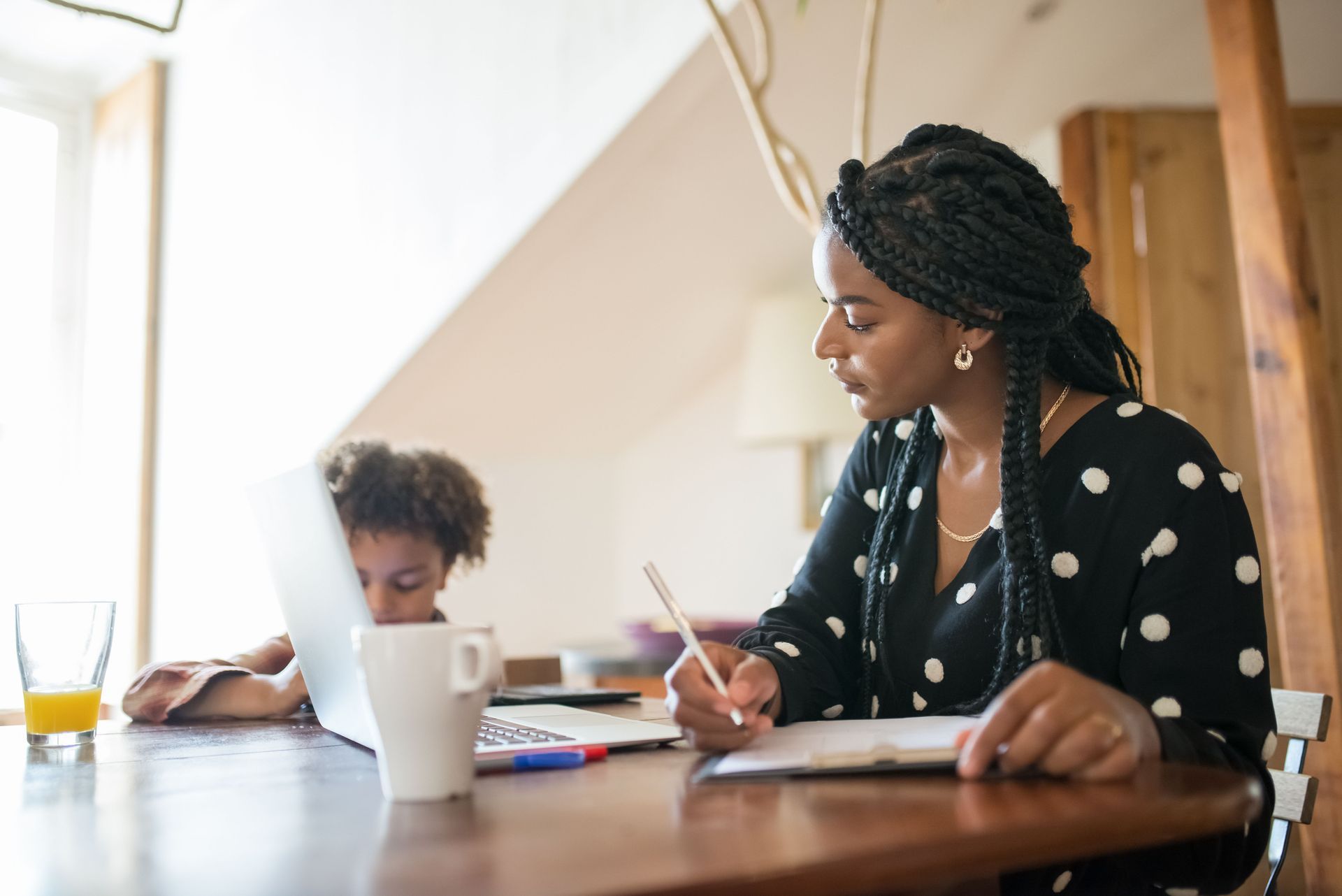 Woman and child writing at a wooden table in a bright kitchen