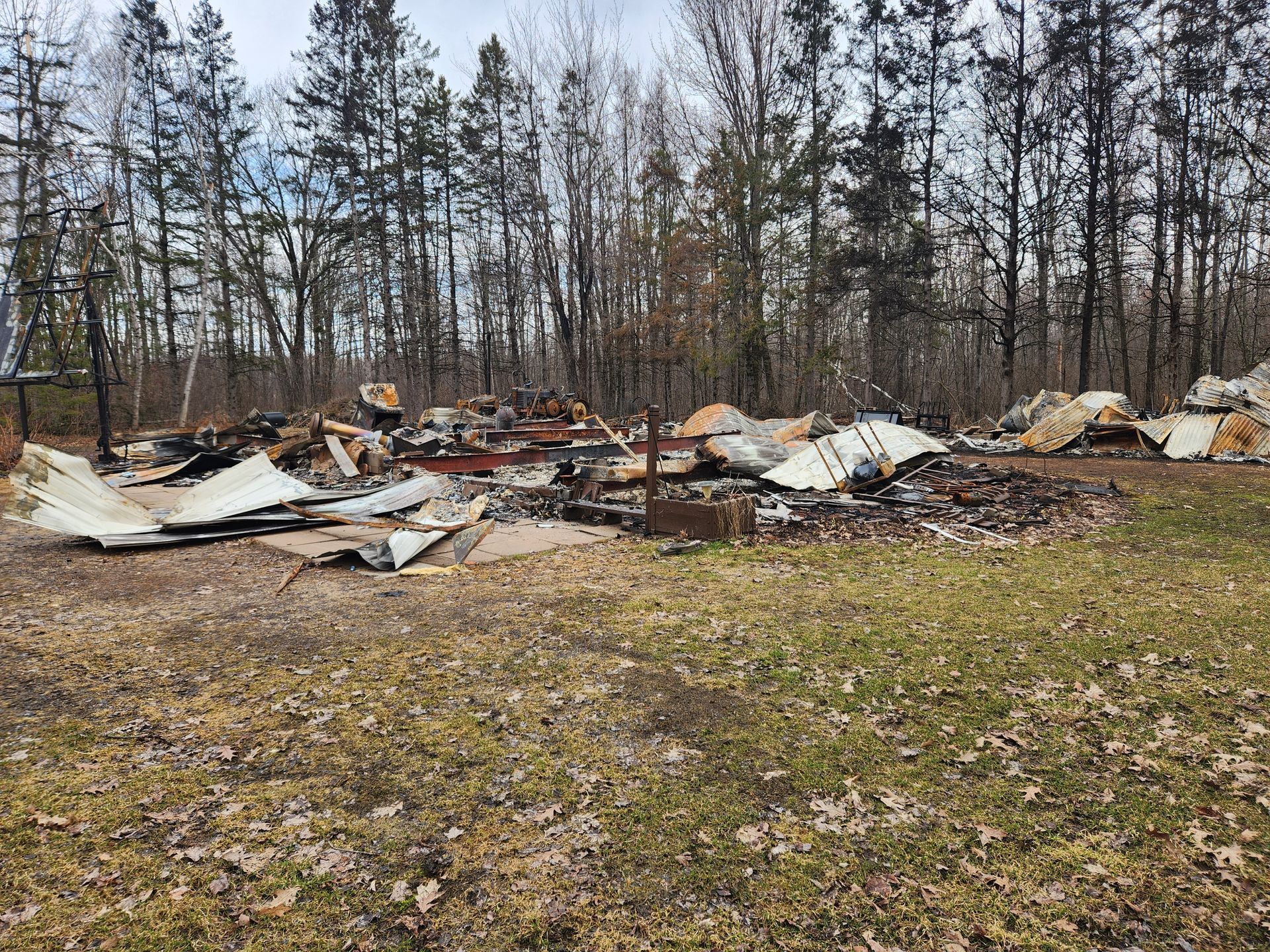 Debris and rubble of a burnt building, with charred materials and collapsed structure in a grassy field.