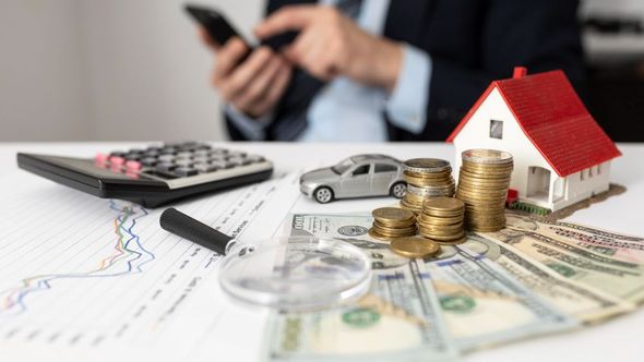 A man is sitting at a table with a house , coins , a car , and a calculator.