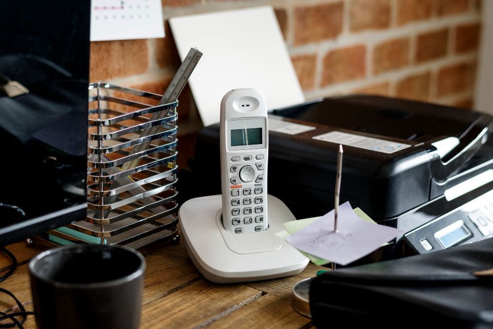 A telephone is sitting on a desk next to a printer.