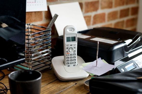 A telephone is sitting on a desk next to a printer.