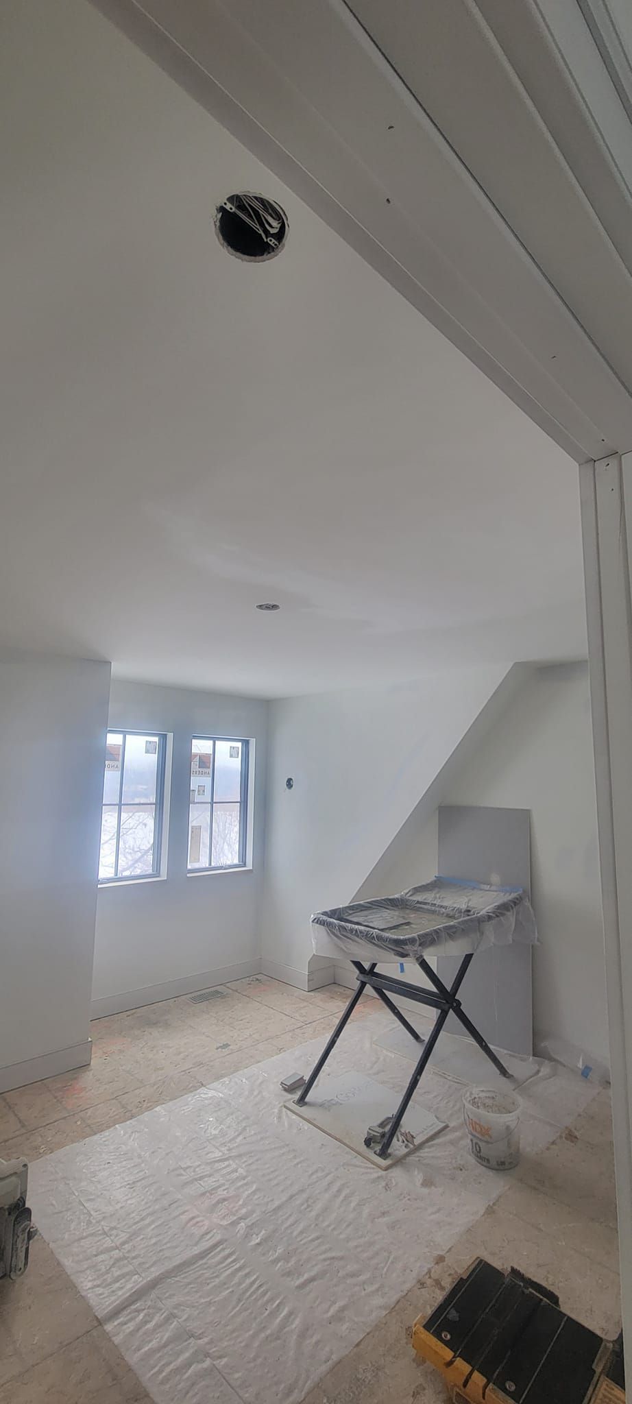 Interior room, freshly painted white. A folding table and stairs are visible. A window provides natural light.