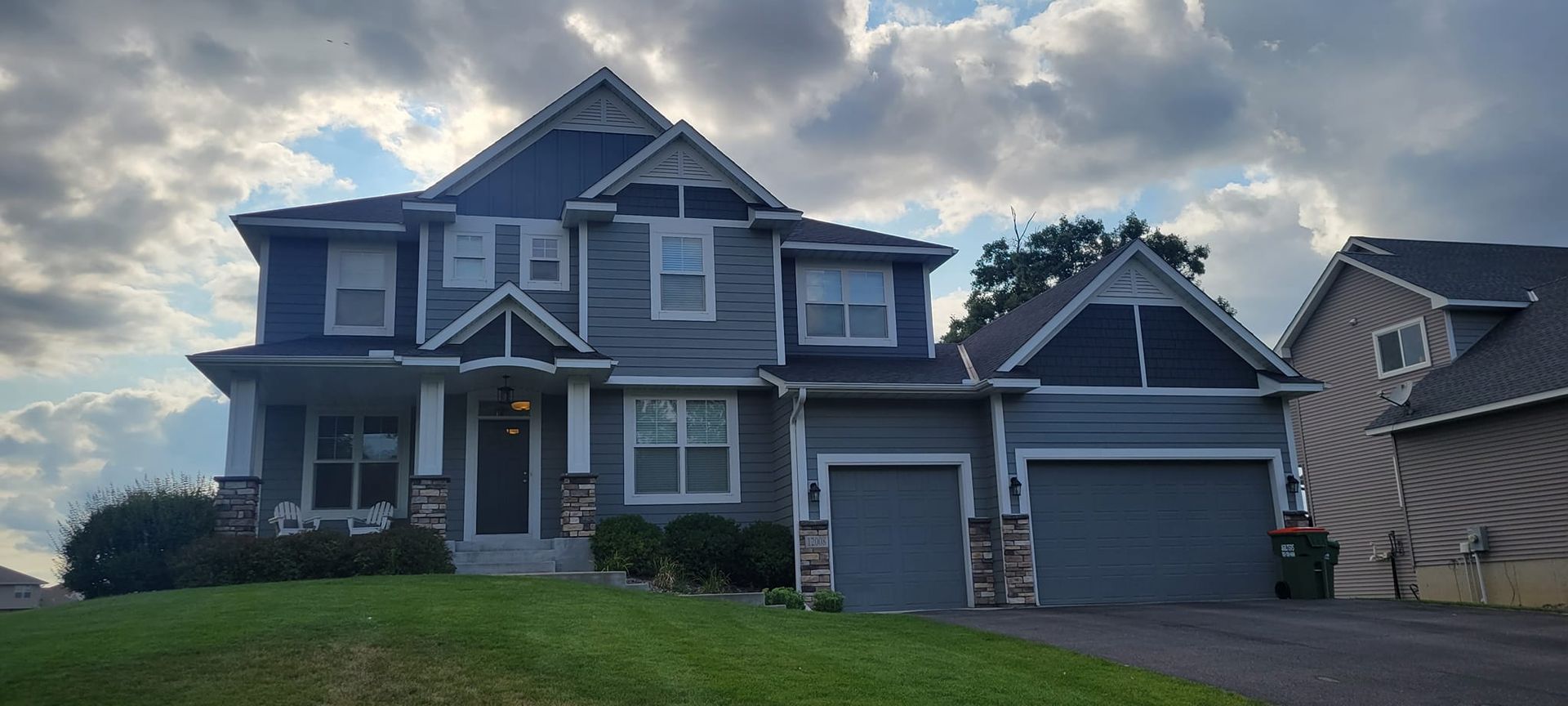 A two-story blue house with a green lawn under a cloudy sky.