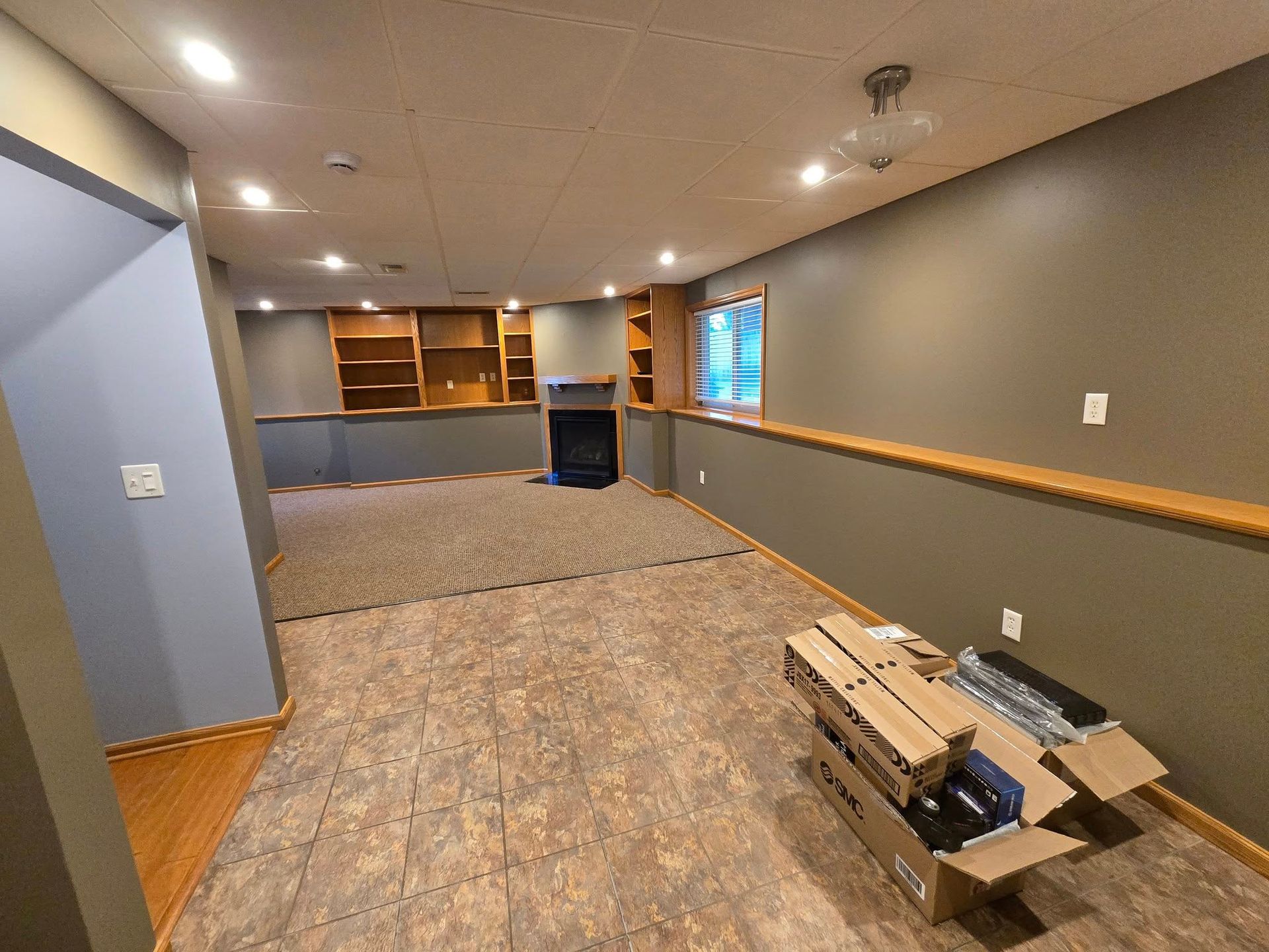 Basement interior with brown and gray walls, built-in shelving, fireplace, and linoleum flooring.