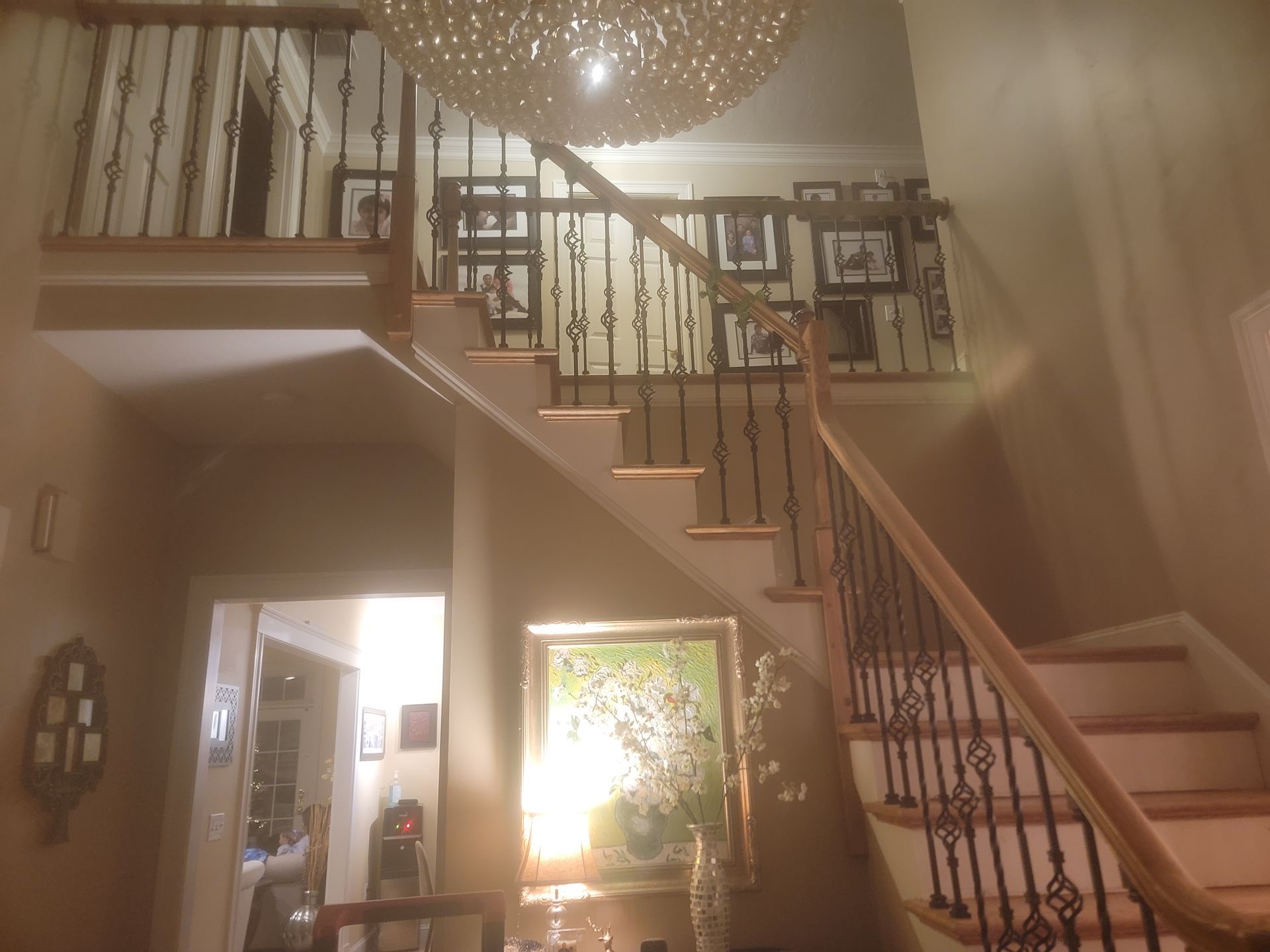 Interior staircase with ornate iron railings, chandelier, and warm lighting leading to a mezzanine.
