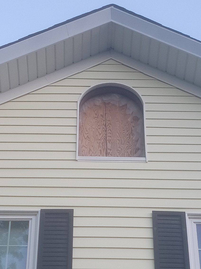 Boarded arched attic window on a beige house exterior with dark shutters.