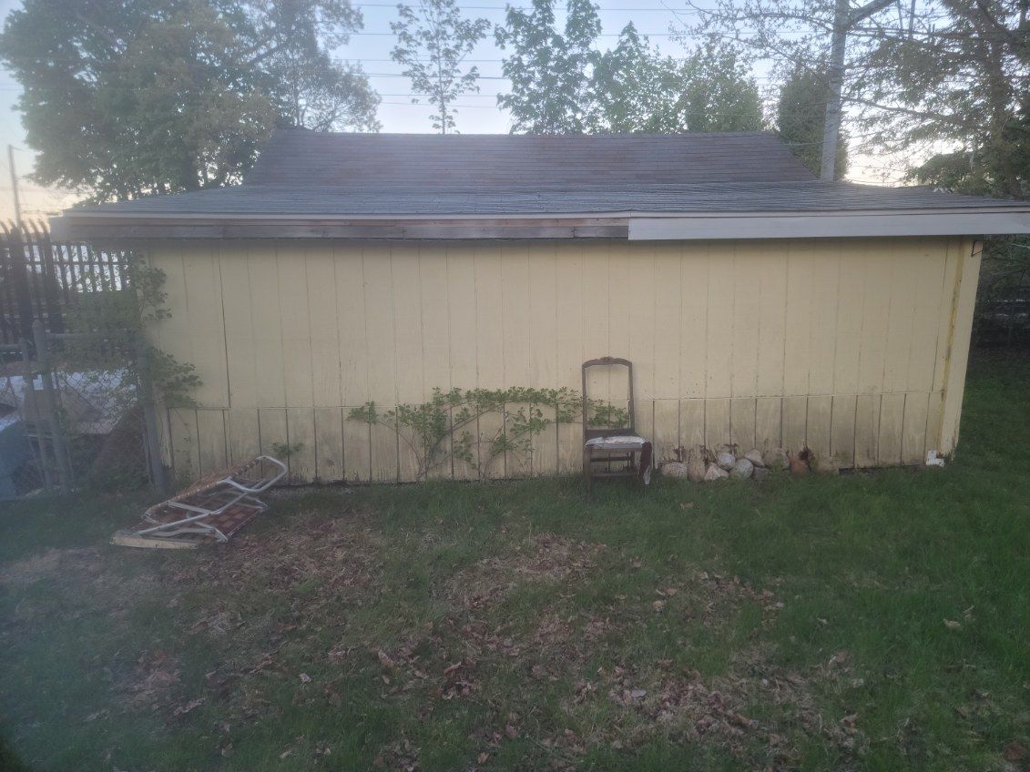 Yellow shed with a dark roof in a grassy yard at dusk, with a small ladder in front.