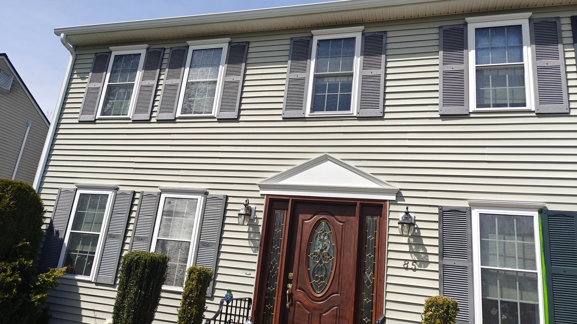 Front view of a two-story beige house with white shutters and a red front door