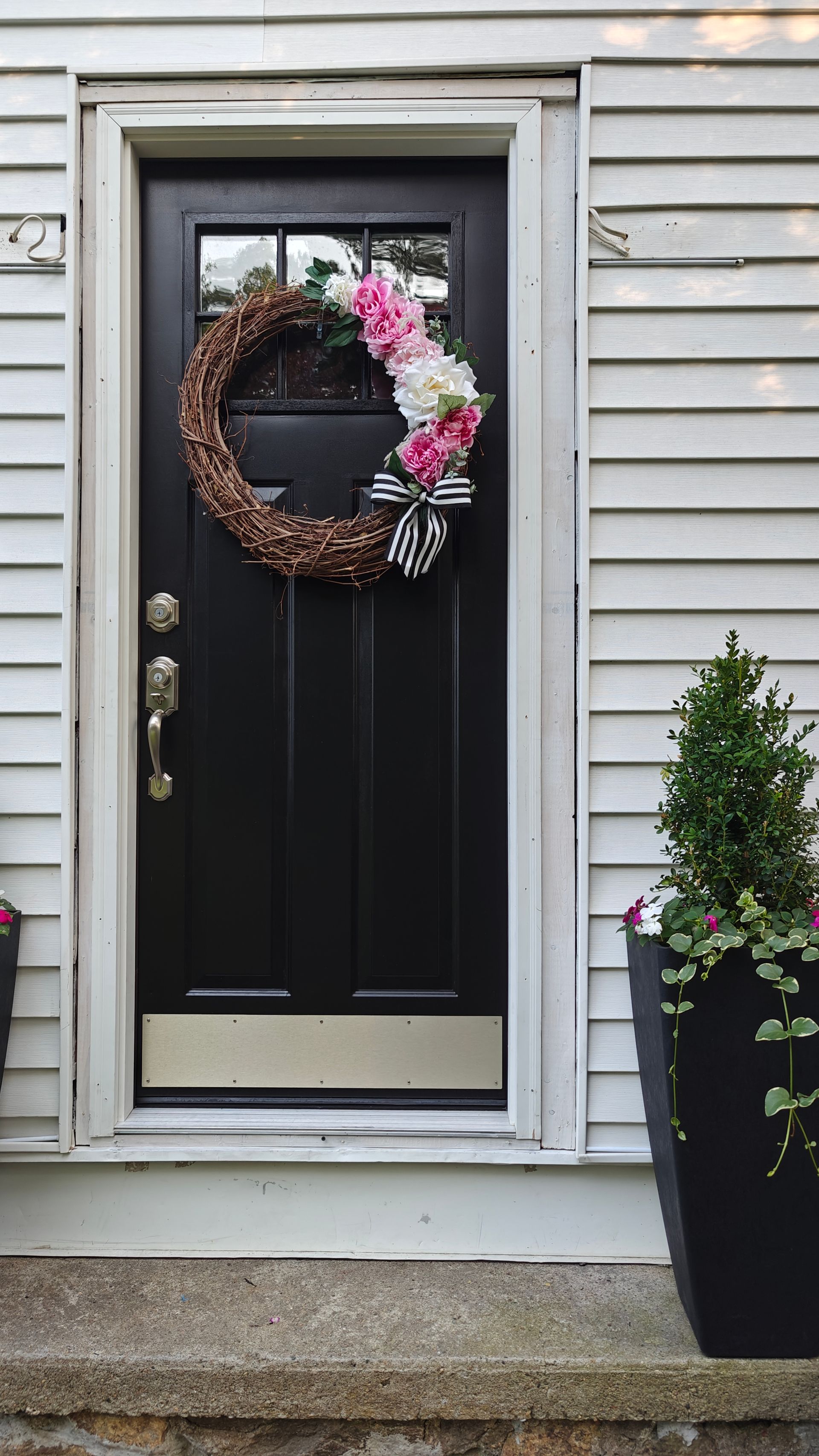 Front door with a wreath, beside a potted plant on a gray house exterior.