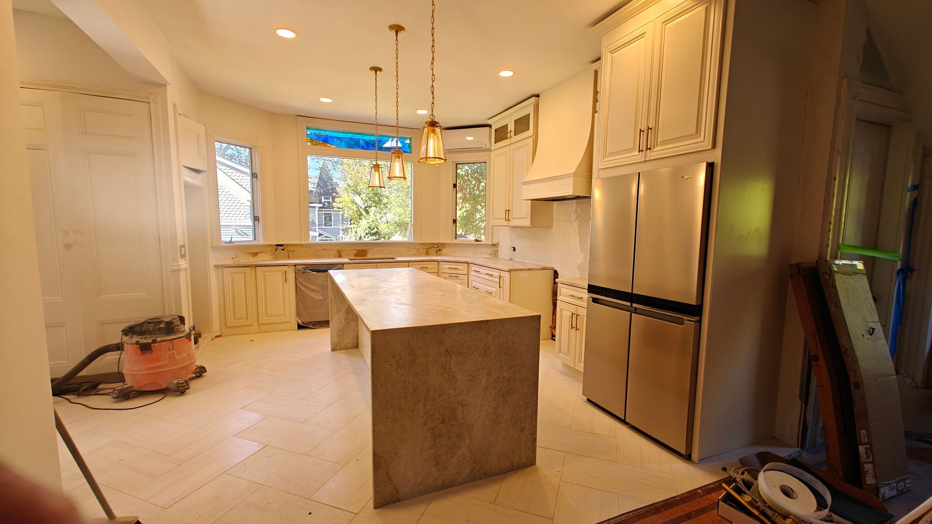 Kitchen renovation with island, white cabinets, stainless fridge, and unfinished floor under warm lighting