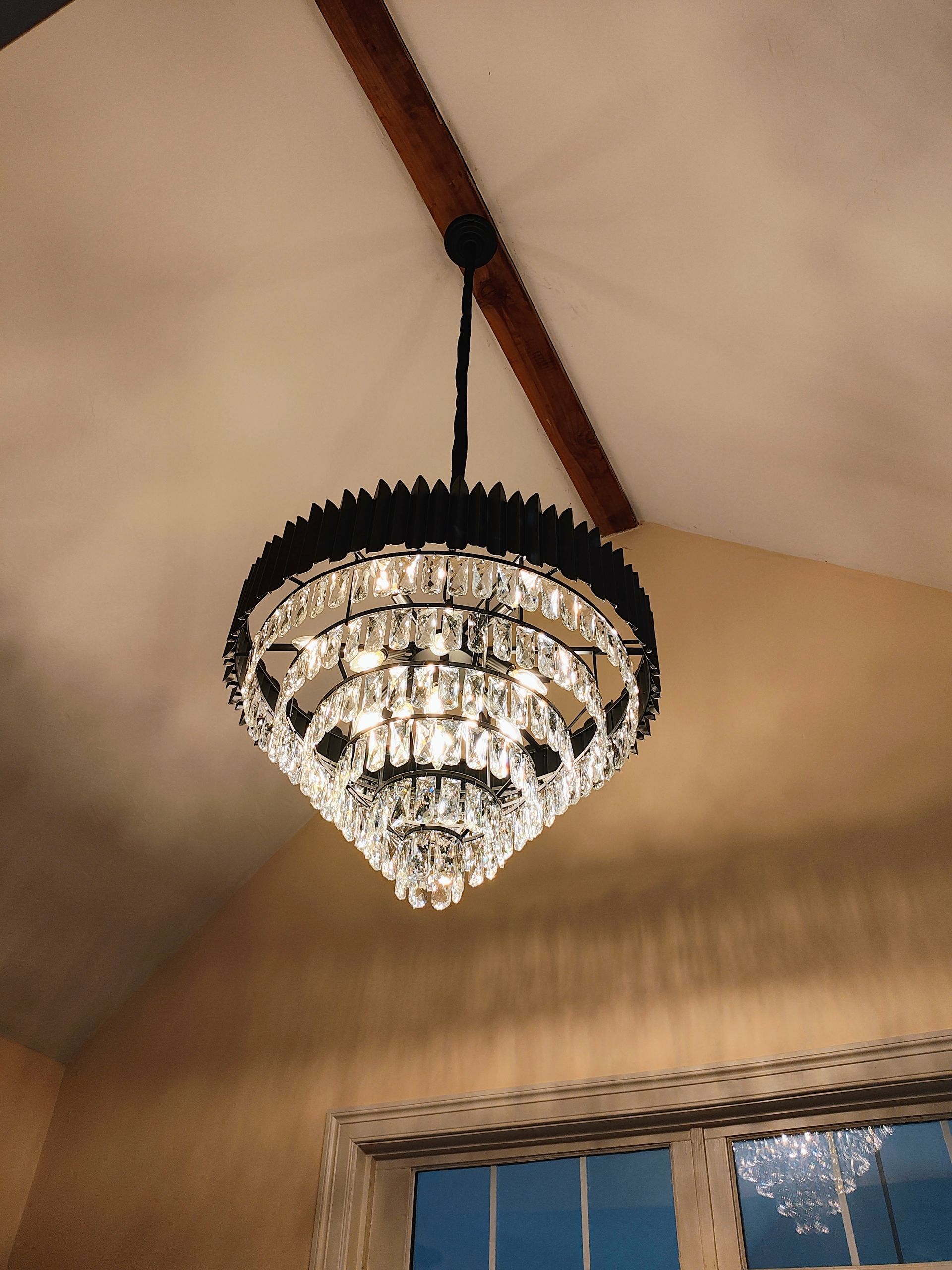Crystal chandelier hanging from a vaulted ceiling with exposed wooden beams.